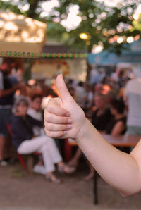 Cropped hand of woman gesturing thumbs up sign in city