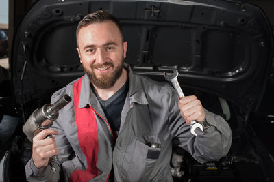 Portrait of male mechanic holding tools while sitting on chair