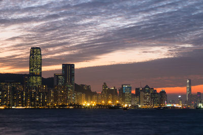 Illuminated buildings by sea against sky during sunset