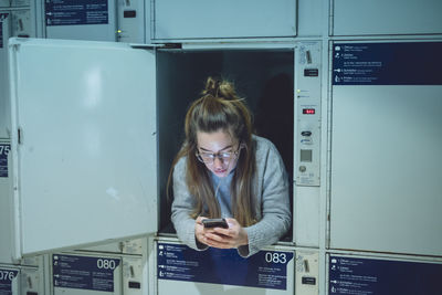 Young woman using phone in locker