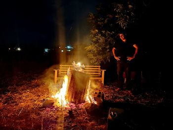 Man standing against illuminated fire at night
