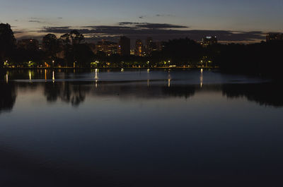 Scenic view of lake by illuminated city against sky at dusk