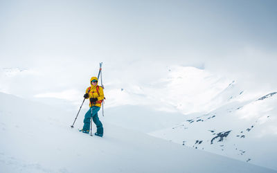 A woman smiles while hiking up a slope with skis on her back