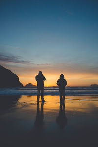 Silhouette of couple standing at beach during sunset