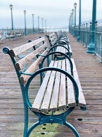 Empty benches on footpath by pier against sky