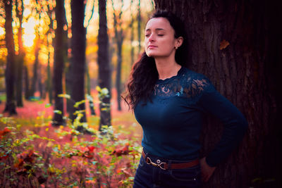 Young woman looking away while standing on tree trunk in forest