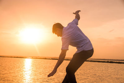 Side view of young woman standing against sea during sunset