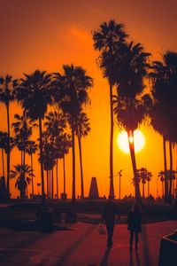 Silhouette people by palm trees against orange sky