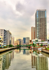 Modern buildings by river against sky in city