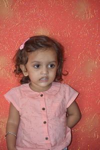 Portrait of cute girl standing against red wall