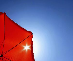 Low angle view of red parasol against clear blue sky