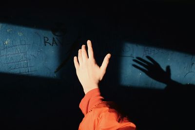 Cropped hand of woman gesturing against blue wall with reflection