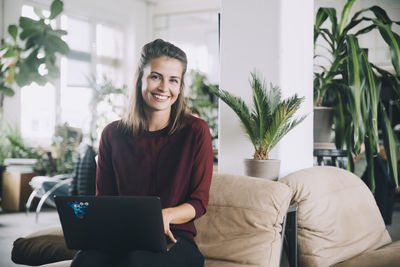 Portrait of smiling young woman sitting on sofa at home