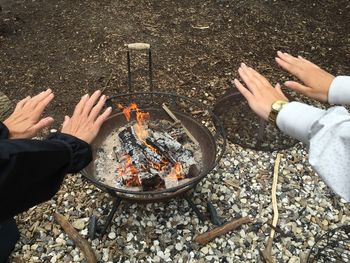 Cropped hands reaching towards fire pit on field