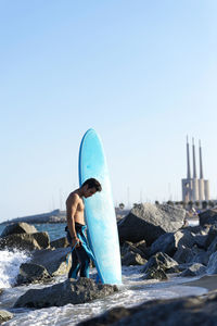 Man standing on rock by sea against clear sky