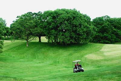 Golf cart moving in green course against trees