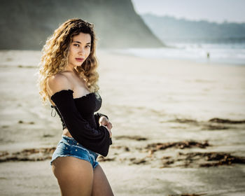 Portrait of beautiful woman standing at beach against sky