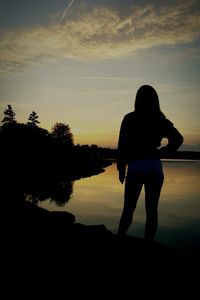 Silhouette woman standing by lake against sky during sunset