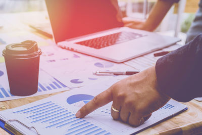 Midsection of colleagues analyzing charts by laptop on office desk