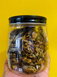 Close-up of hand holding glass jar against yellow background