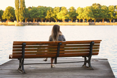 Rear view of woman sitting on bench by lake