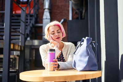 Serene informal female sitting at table with eco friendly cup with hot beverage in city on sunny day