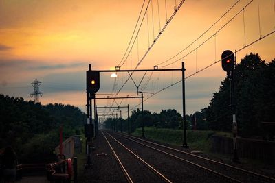 Railroad tracks by silhouette trees against sky at sunset