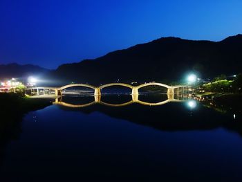 Illuminated lake by mountains against clear blue sky at night