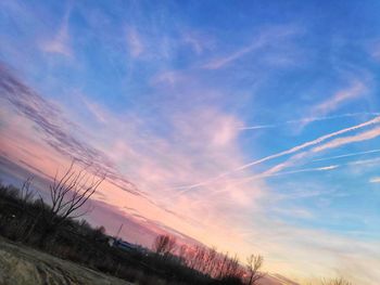 Low angle view of vapor trails in sky at sunset