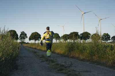 Technician walking on field path at a wind farm with climbing equipment