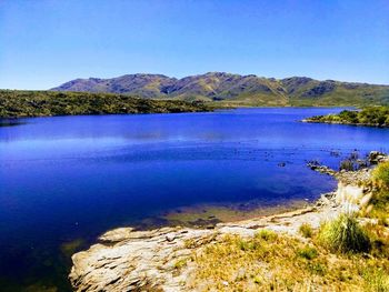 Scenic view of lake and mountains against clear blue sky