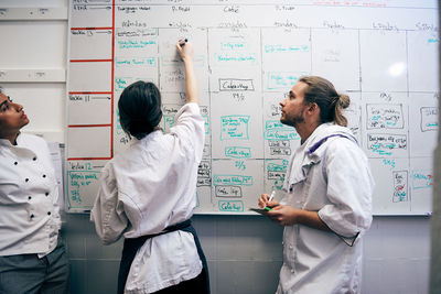 Female chef writing menu on whiteboard by colleagues in kitchen