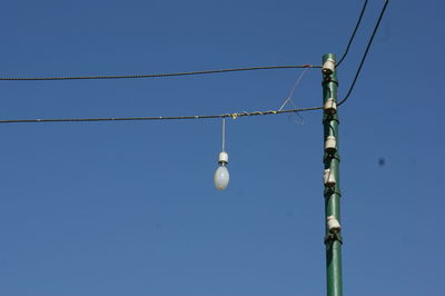 Low angle view of light bulb hanging on power line against clear blue sky