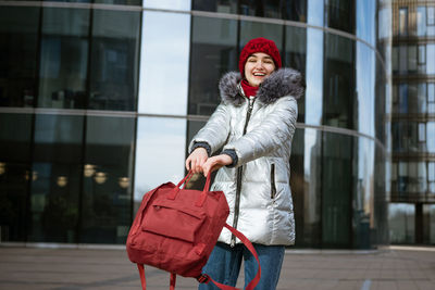 Young happy woman in a warm jacket with a backpack travels the cities