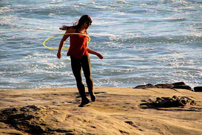 Girl exercises with hulahoop on a cliff overlooking the ocean.