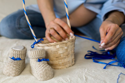 A pregnant woman is preparing a gift for her unborn child. puts baby booties in a wicker basket.