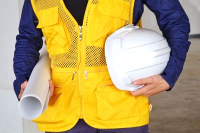 Midsection of architect holding hardhat and blueprint