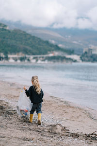 Rear view of woman standing on beach against sky