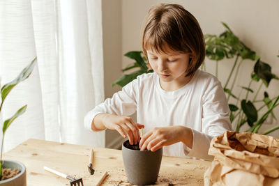 A cute little girl is planting or transplanting plants in a flower pot at home. hobby 