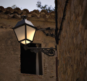 Illuminated lamp mounted on wall at dusk