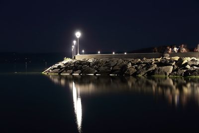 Illuminated rock by sea against clear sky at night