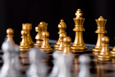 Close-up of golden chess pieces on board against black background