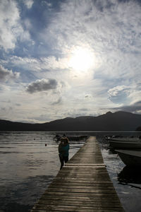 Rear view of woman standing on lake against sky