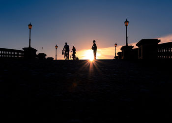 Silhouette people on street against orange sky