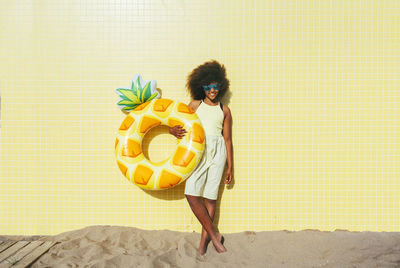 Smiling girl wearing sunglasses holding swimming float at beach