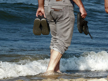 Low section of man holding surfboard on beach