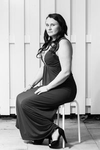 Portrait of woman sitting on stool against fence