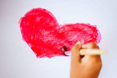 Cropped hand of child painting red heat shape on white paper