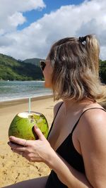 Woman holding coconut at beach against sky