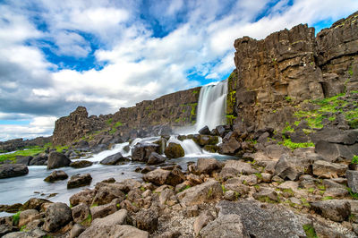 Scenic view of waterfall by rocks against sky